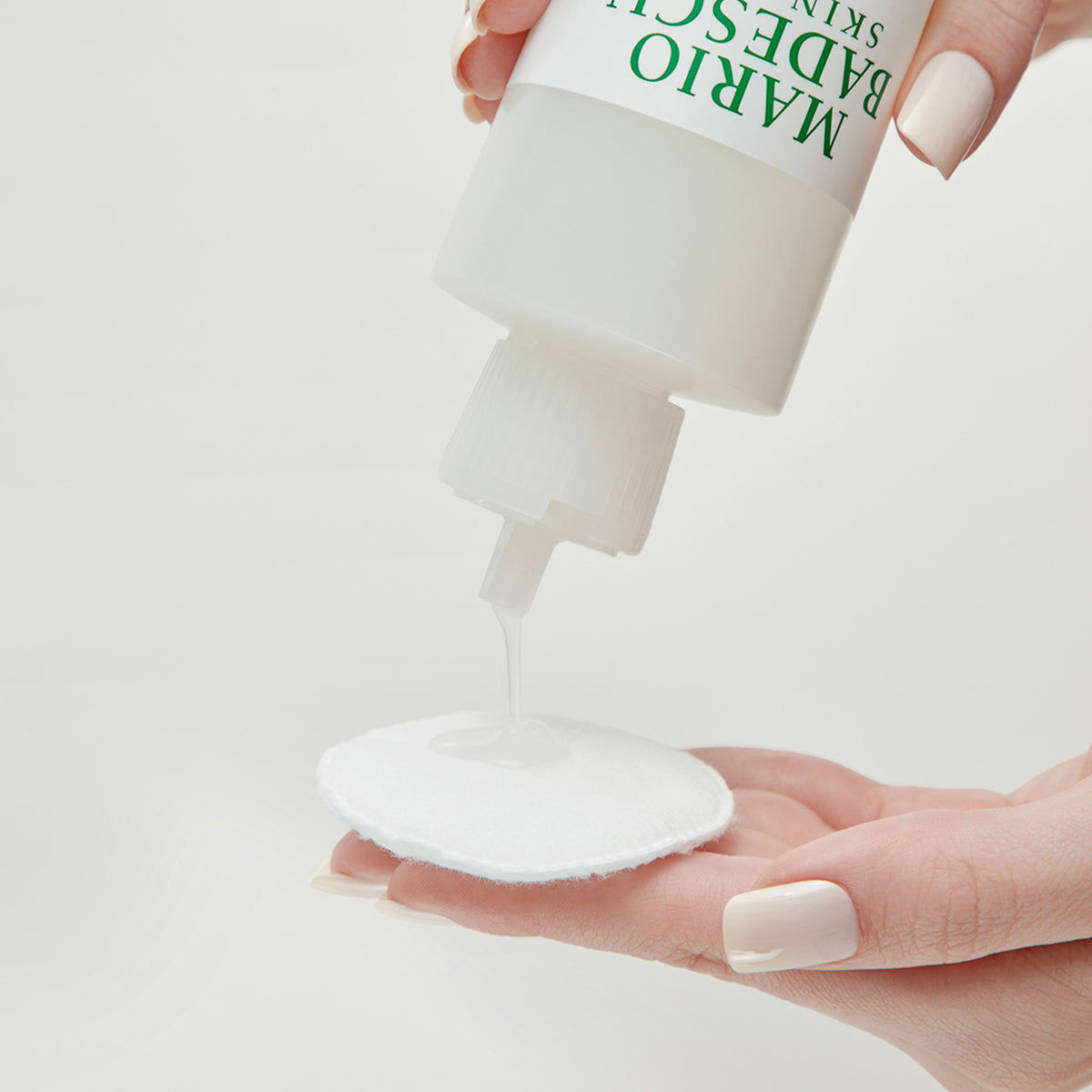 Eine Hand gießt Mario Badescu Hydrating Glow Toner aus einer weißen Flasche auf ein rundes Wattepad.