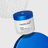 Runde Dose der Medicube Zero Pore Pad 2.0 mit blauem Deckel, auf hellgrauem Hintergrund, daneben ein vergrößertes Texturdetail eines Pads.