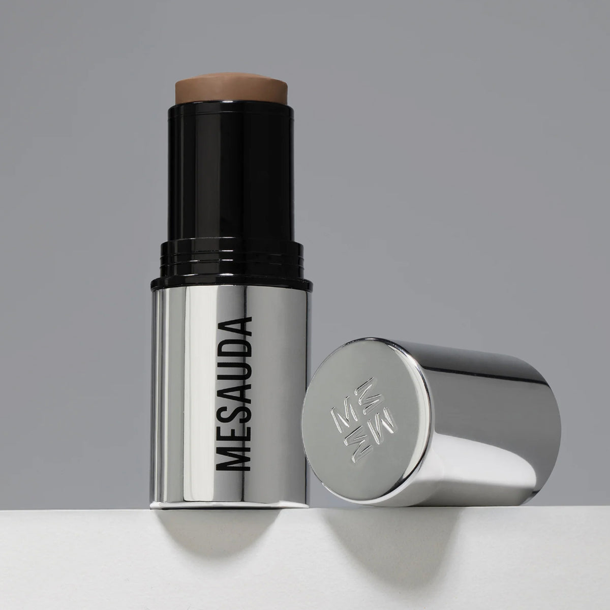 Der silberne Make-up-Stift The Mood Contrast 102 Medium von Mesauda neben silberner Kappe auf grauem Hintergrund.