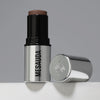 Der silberne Make-up-Stift The Mood Contrast 103 Dark von Mesauda neben silberner Kappe auf grauem Hintergrund.