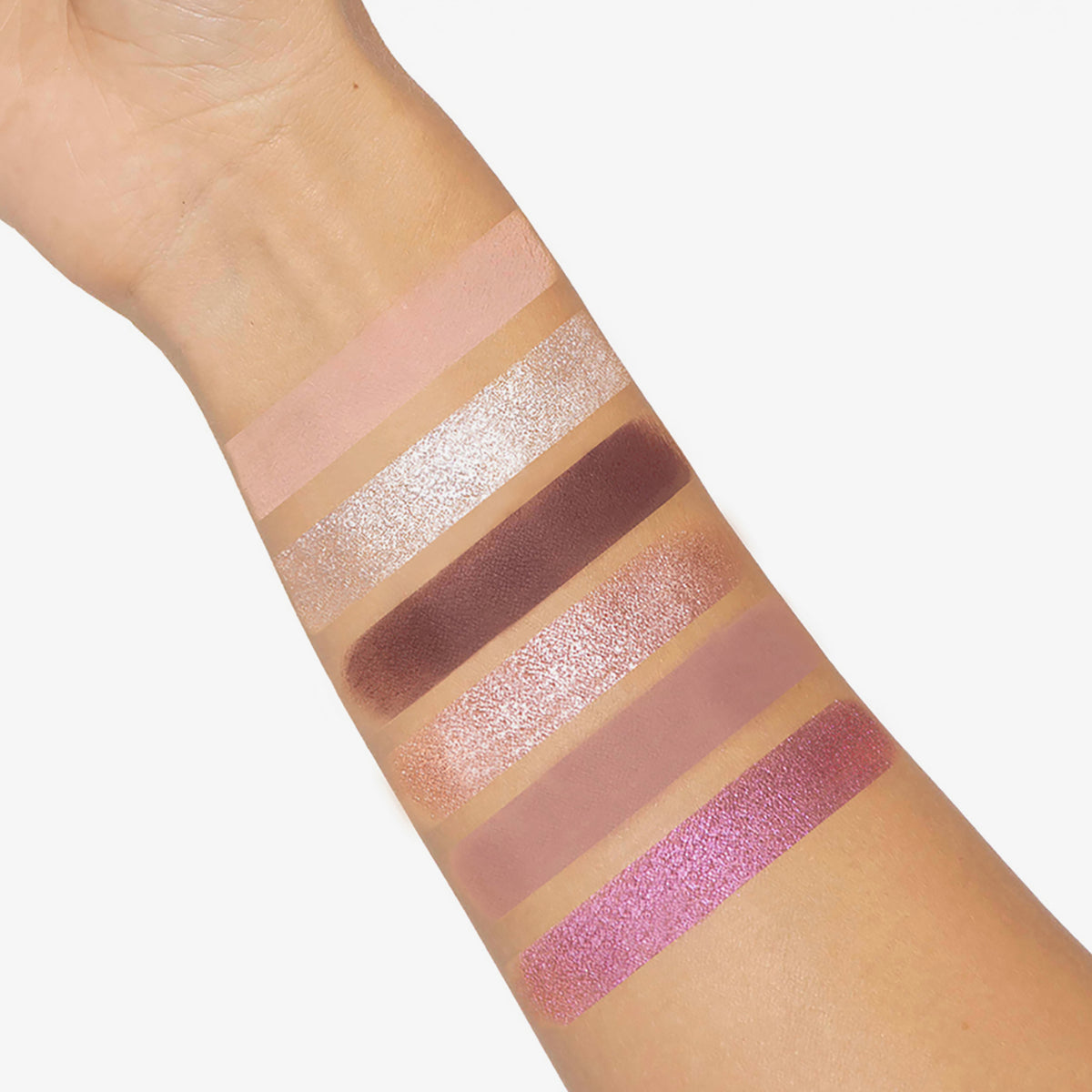 Ein Arm zeigt sechs Swatches von schimmernden und matten Lidschatten aus der Palette Bare Harmony 2.0 von Mesauda Beauty.
