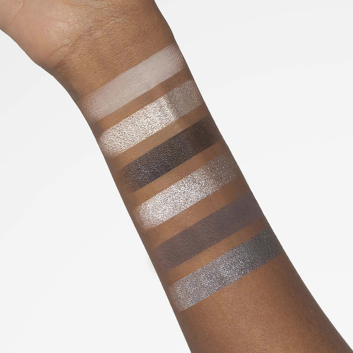 Ein Arm zeigt sechs Swatches der Bare Harmony 2.0 Palette von Mesauda Beauty, die eine Mischung aus schimmernden und matten Lidschattenfarben enthält.