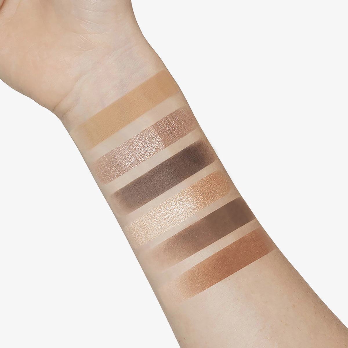 Ein innerer Unterarm zeigt sechs Swatches der nudefarbenen und braunen Bare Harmony 2.0 Lidschattentöne von Mesauda Beauty.