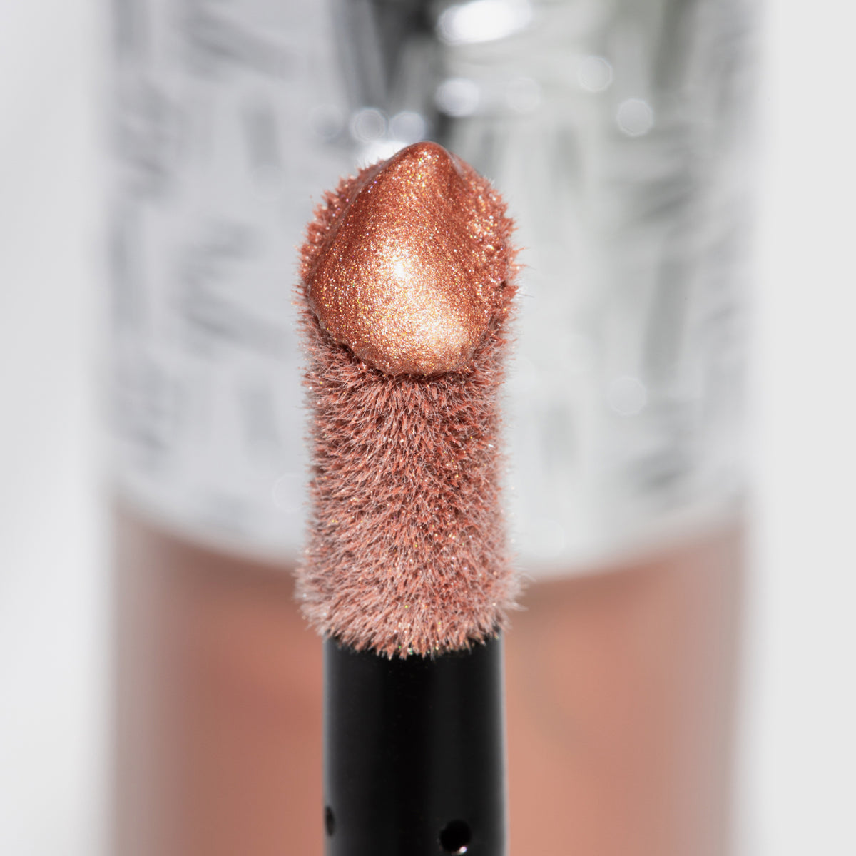 Nahaufnahme des Highlighter-Applikators; darauf ein Tropfen Flush of Light Blossom Shine mit strukturierter silber Kappe im Hintergrund.