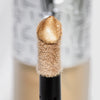 Nahaufnahme des Highlighter-Applikators; darauf ein Tropfen Flush of Light Golden Hour mit strukturierter silber Kappe im Hintergrund.