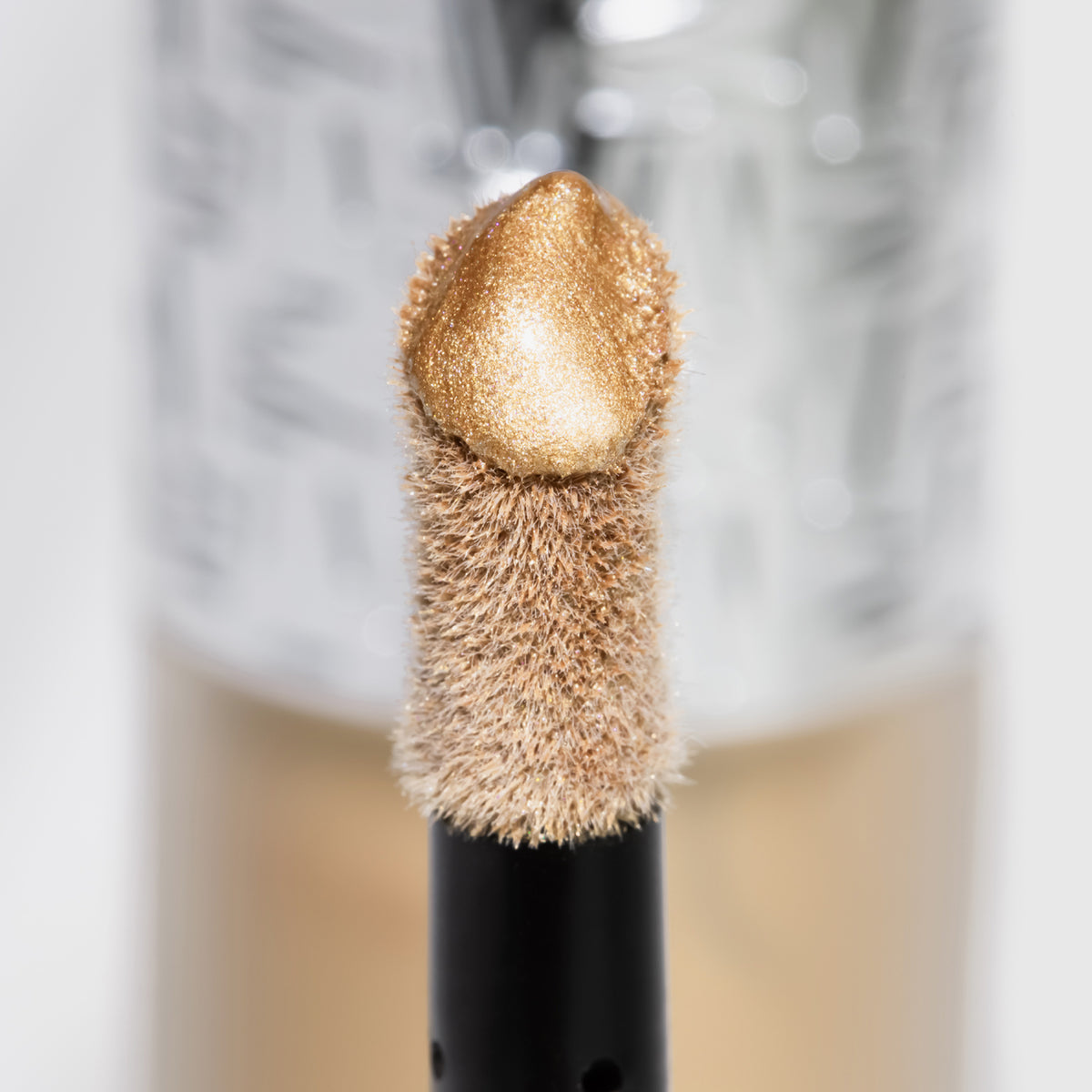 Nahaufnahme des Highlighter-Applikators; darauf ein Tropfen Flush of Light Golden Hour mit strukturierter silber Kappe im Hintergrund.