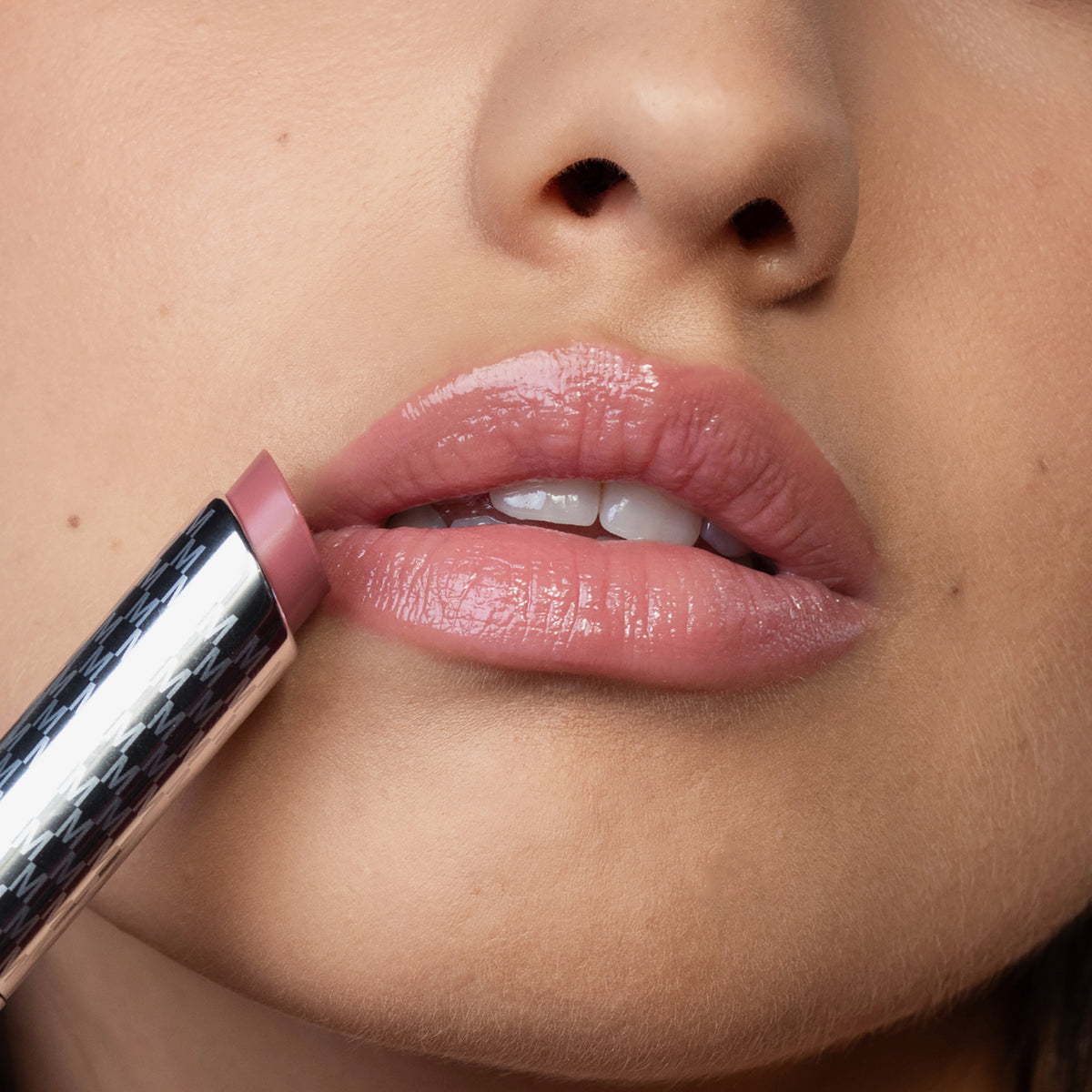 Nahaufnahme der glänzenden Lippen einer Frau, die den rosa Lippenstift Hydramorphosis von Mesauda Beauty an den Mund hält.