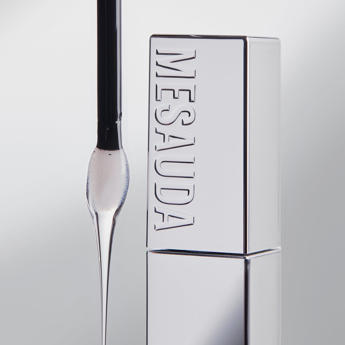 Ein Applikator mit abfließendem Produkt neben einer silbernen Mesauda Beauty LIP PHENOM™ Flasche auf einem hellen Hintergrund.