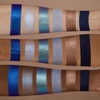 Drei Arme mit unterschiedlichen Hauttönen zeigen blaue, silberne, bronzene und marineblaue Lidschattenmuster aus der Cutie-Palette.