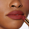 Nahaufnahme einer Person mit einem dunkleren Hautton, die sich den Beyond Blurry Lipstick, in der Farbe afrodité, auf die Lippen aufträgt.