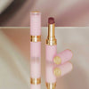 Zwei Beyond Blurry-Lippenstifte in Pink und Gold, einer offen und einer geschlossen, präsentiert auf einer reflektierenden Oberfläche.