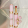 Zwei Beyond Blurry-Lippenstifte in Pink und Gold, einer offen und einer geschlossen, präsentiert auf einer reflektierenden Oberfläche.