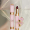 Zwei Beyond Blurry-Lippenstifte in Pink und Gold, einer offen und einer geschlossen, präsentiert auf einer reflektierenden Oberfläche.