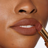 Nahaufnahme einer Person mit einem dunkleren Hautton, die sich den Beyond Blurry Lipstick, in der Farbe saint, auf die Lippen aufträgt.