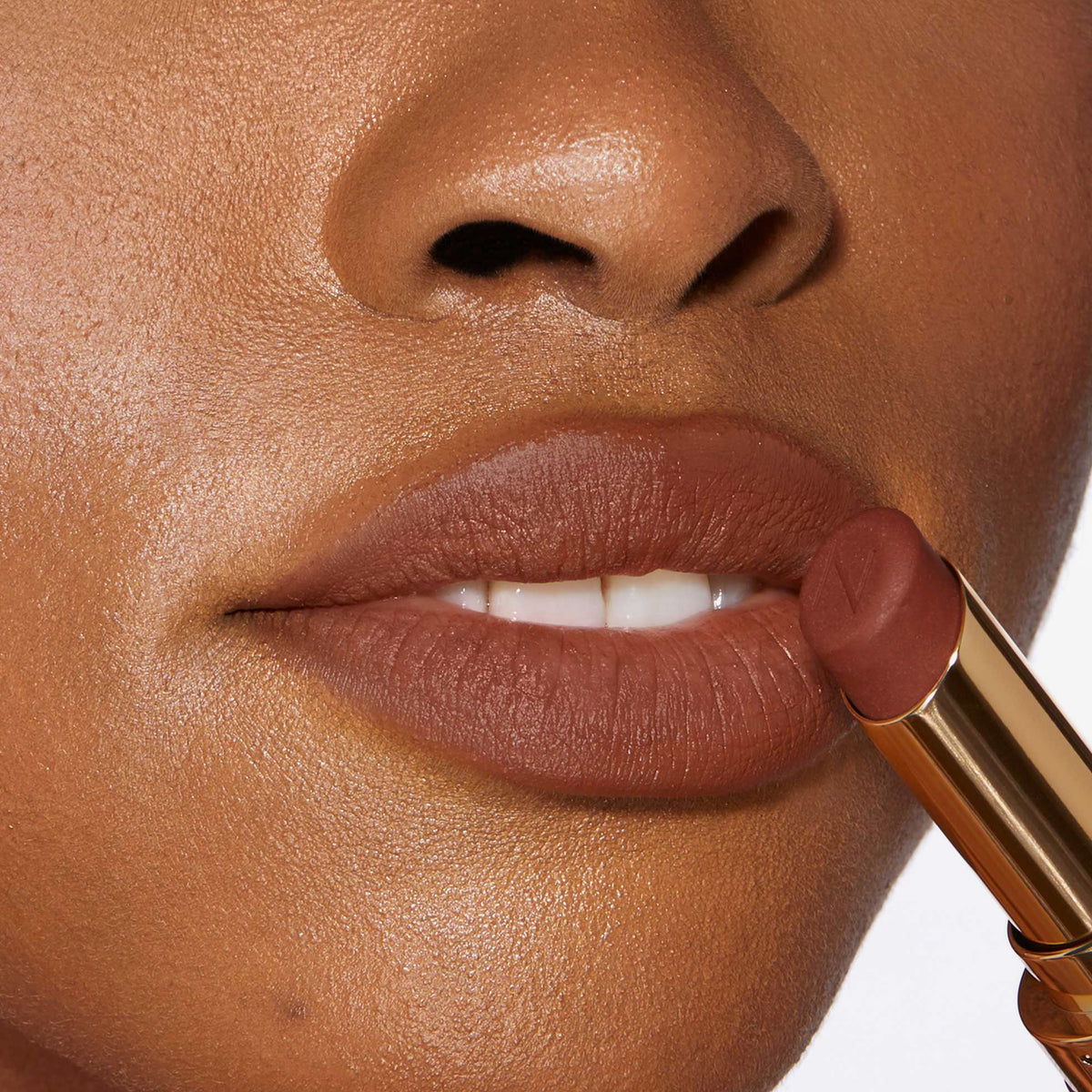 Nahaufnahme einer Person mit einem dunkleren Hautton, die sich den Beyond Blurry Lipstick, in der Farbe saint, auf die Lippen aufträgt.