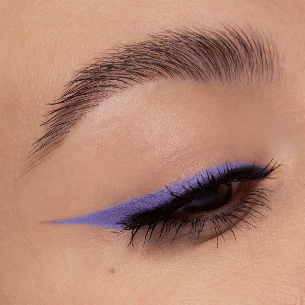 Nahaufnahme eines Auges mit kräftigem violettem Wing Liner und definierten Wimpern unter Verwendung von NABLA Cosmetics Cupids Arrow Longwear Stylo.