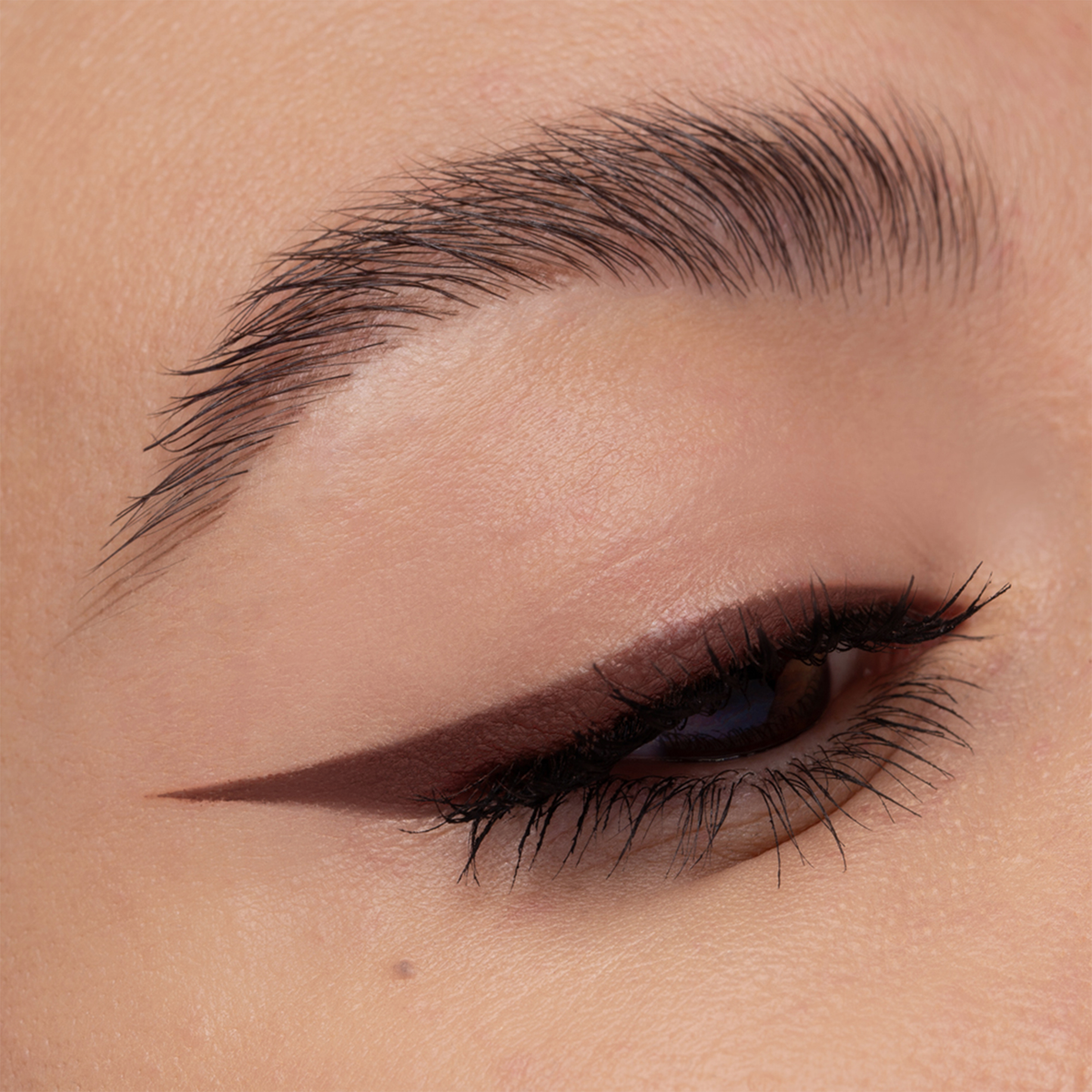 Eine Nahaufnahme eines geschlossenen Auges mit kühnem Wing Liner und einer gepflegten Augenbraue, die mit NABLA Cosmetics Cupids Arrow Longwear Stylo kreiert wurde.