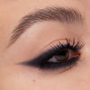 Nahaufnahme eines Auges mit intensivem, rauchigem Lidstrich in dunklem Anthrazit, der nach außen spitz ausläuft. Die Wimpern sind schwarz und geschwungen.