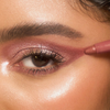 Nahaufnahme eines Auges mit schimmerndem Rosé-Make-up. Ein roségoldener Lidschattenstift betont den äußeren Augenwinkel für einen strahlenden Look.