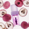 Eine Flasche Lip Candy Oil, umgeben von ganzen und halbierten roten Trauben auf weißem Hintergrund.