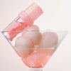 Lip Candy Oil sitzt auf Eiskugeln in einem Martini-Glas, das mit hellrosa Flüssigkeit gefüllt ist.