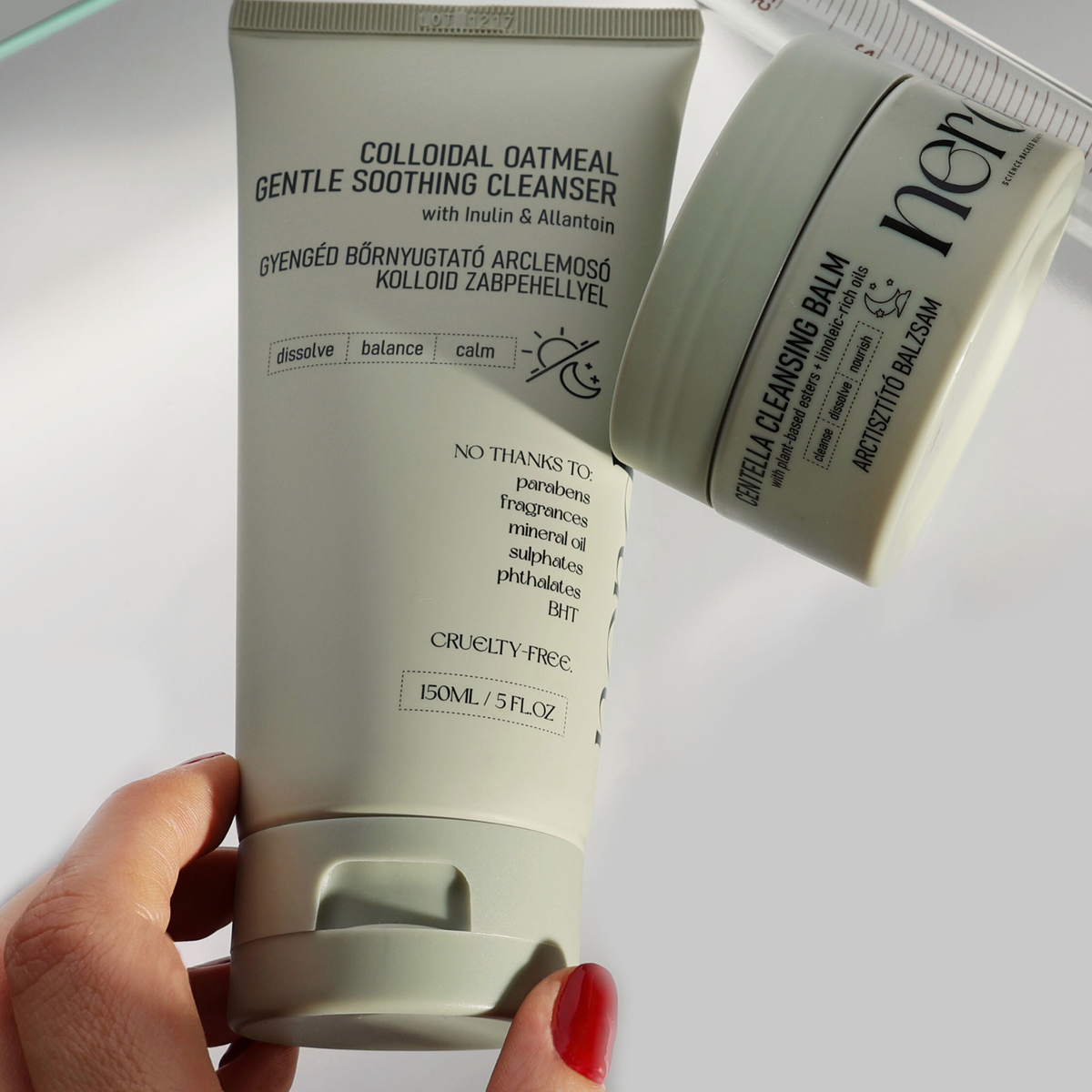 Eine Hand hält eine Tube von NERDS. Colloidal Oatmeal Gentle Soothing Cleanser neben einem Tiegel Centella Cleansing Balm.
