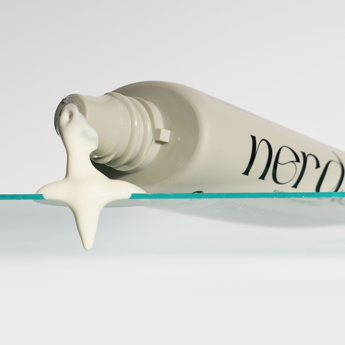 Eine Tube der NERDS. Lightweight Hydrate UV Defense Lotion SPF50 spendet die Lotion auf einer Glasoberfläche vor einem weißen Hintergrund.