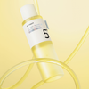 Eine 200-ml-Flasche „Numbuzin No. 5+ Vitamin Boosting Essence Toner“ mit gelber Flüssigkeit vor gelbem Hintergrund.