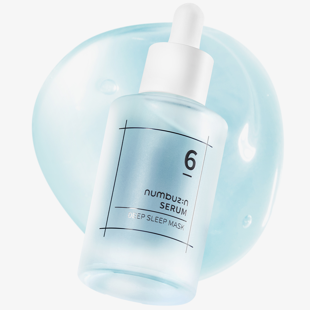 Eine mattierte Flasche „Numbuzin No. 6 Deep Sleep Mask Serum“ mit Tropfer vor einem hellblauen Hintergrund mit Serumflecken.