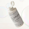 Offene schwebende Flasche N°4 FINE Bond Maintenance Shampoo von OLAPLEX zwischen zwei Blasen.