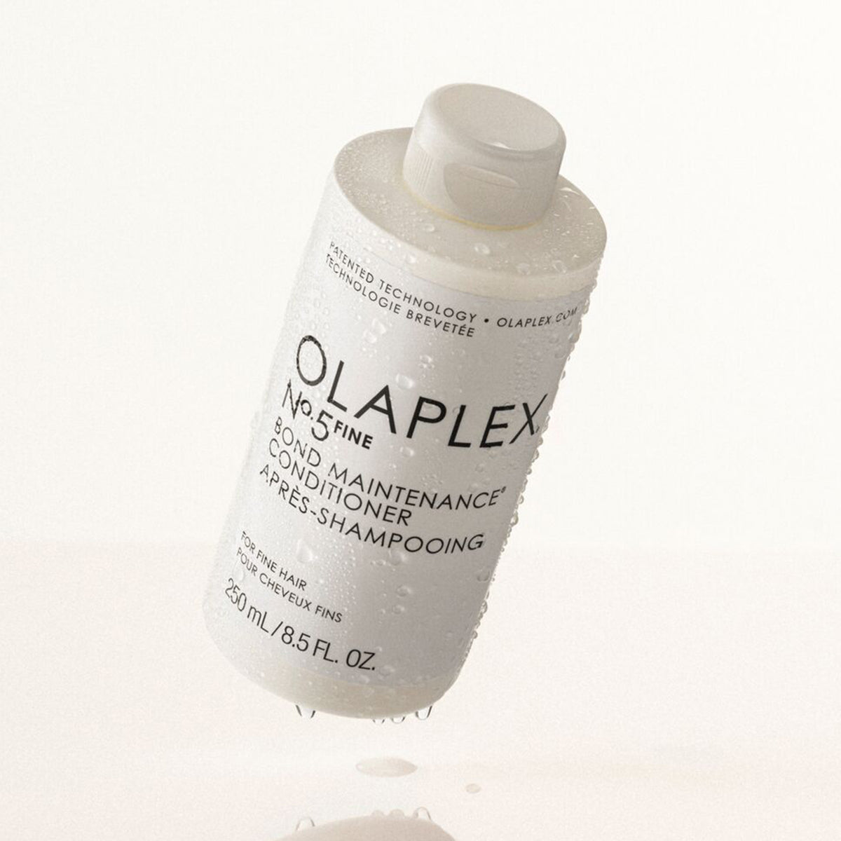 Schwebende nasse Flasche OLAPLEX N°5 FINE Bond Maintenance Conditioner vor weißem Hintergrund.
