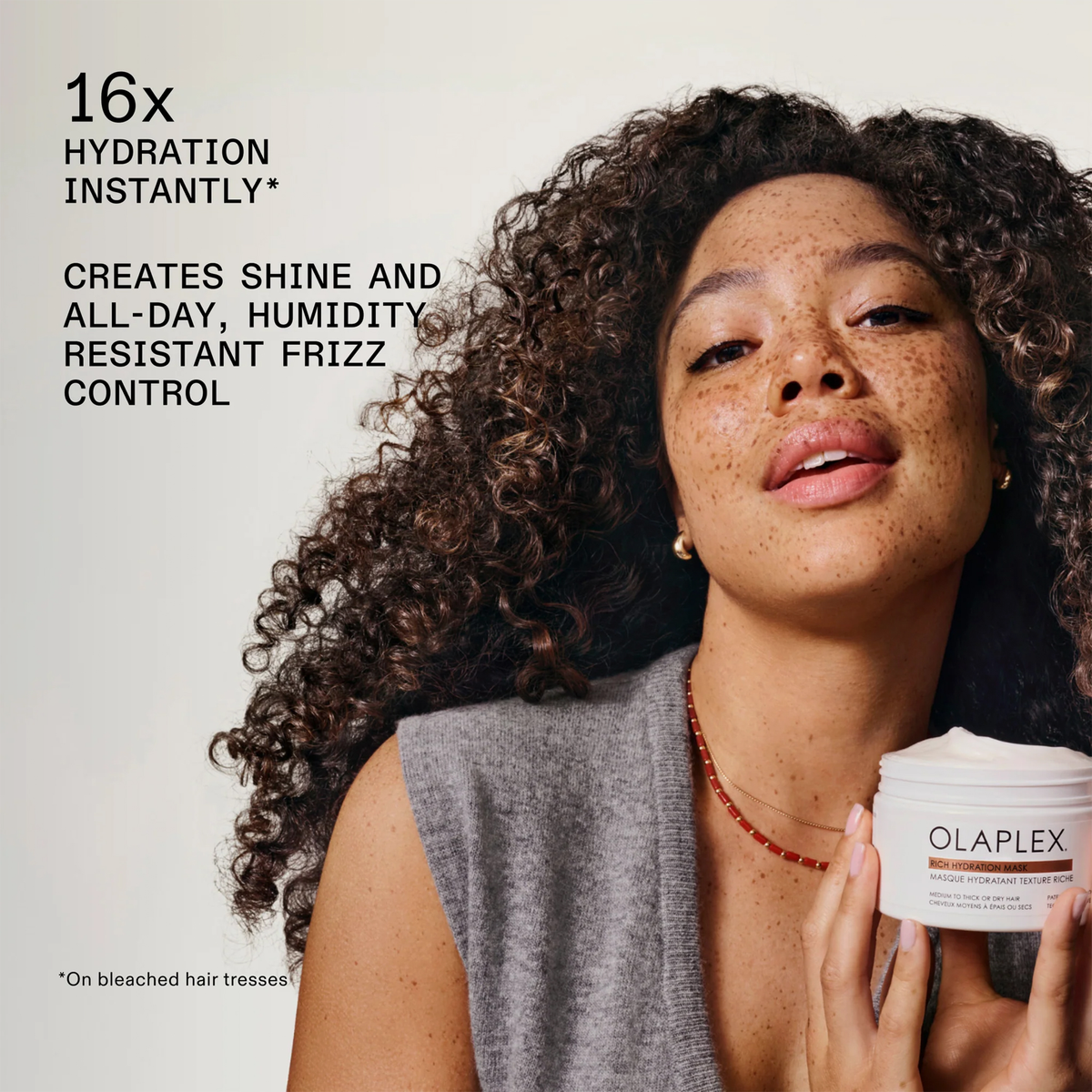 Eine Frau mit lockigem Haar hält einen Tiegel OLAPLEX Rich Hydration Mask in der Hand; daneben Produktvorteile.