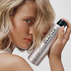 Eine Person hält eine silberne Sprühflasche mit dem Haarspray OLAPLEX Shape Set in der Hand.