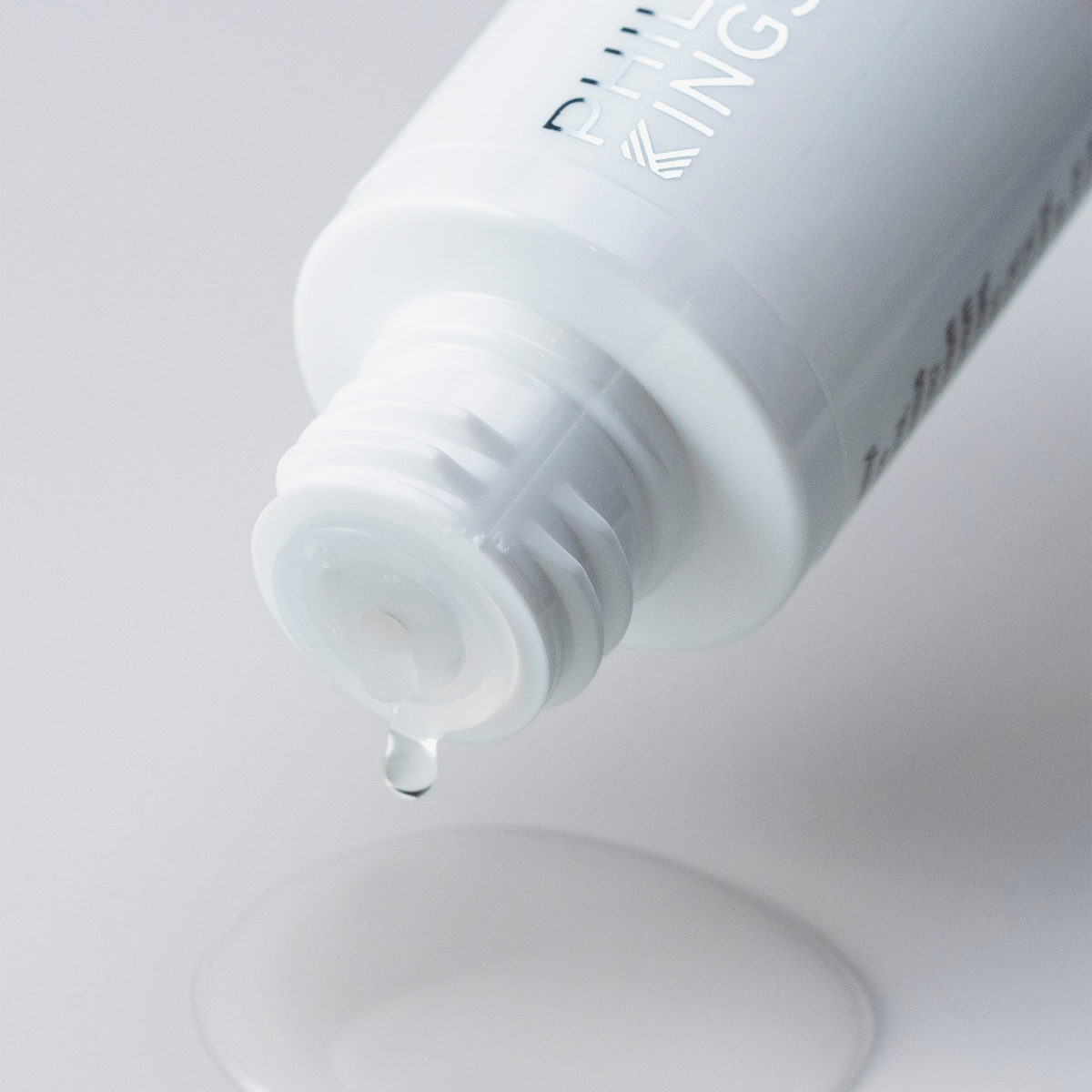 Aus einer weißen Flasche „Philip Kingsley Bond Builder Lipid Shield Oil 30“ tropft eine klare Flüssigkeit auf eine glatte Oberfläche – ein Tropfen fällt herunter.