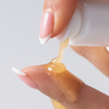Eine Hand mit rosa Fingernägeln drückt „Philip Kingsley Bond Builder Split End Remedy“ aus einer weißen Tube auf einen anderen Finger.