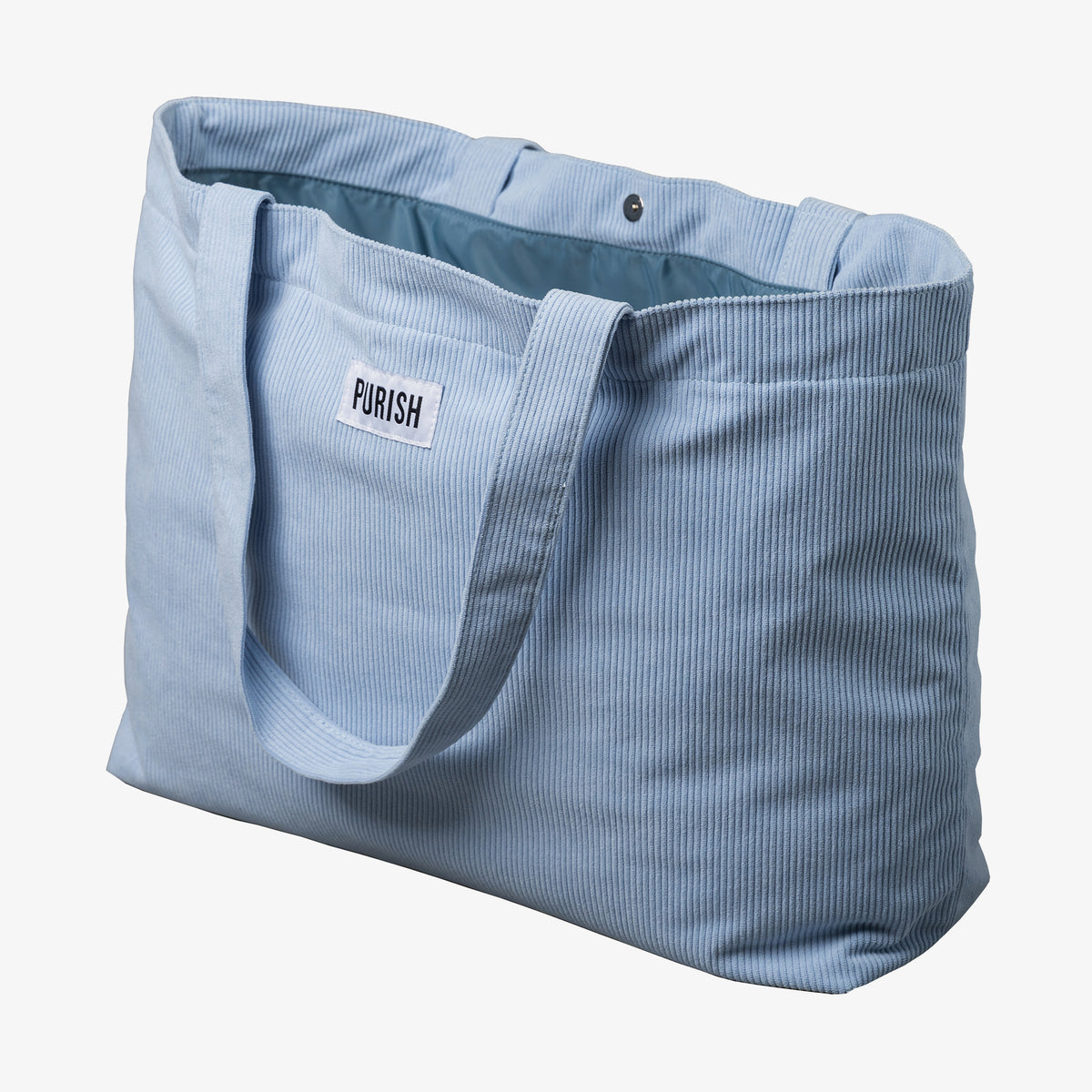 Die geöffnete PURISH Beach Bag ist eine hellblaue Stofftasche mit Tragegriffen und einem „PURISH“-Etikett auf der Vorderseite und einem Druckknopf.