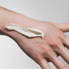 Eine Hand mit einem Streifen von Scandinavian Biolabs Flexible Hybrid Clay auf der Rückseite, vor einem schlichten Hintergrund.