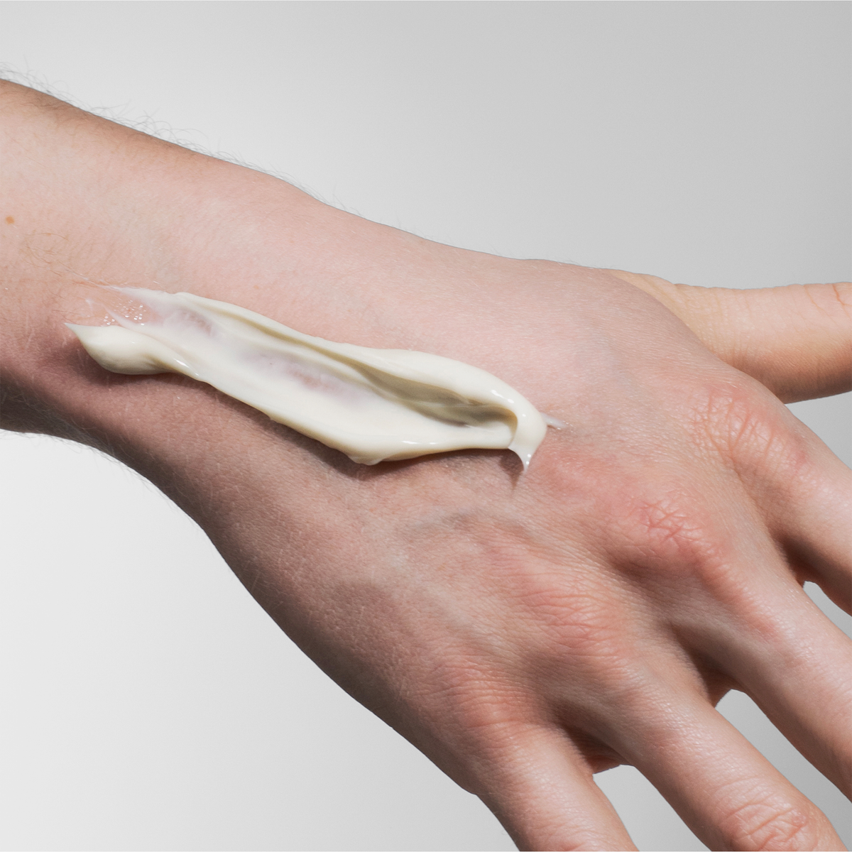 Eine Hand mit einem Streifen von Scandinavian Biolabs Flexible Hybrid Clay auf der Rückseite, vor einem schlichten Hintergrund.