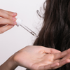 Eine Person trägt Scandinavian Biolabs Hair Protection Oil aus einem Glastropfer auf ihre Handfläche in der Nähe von langem, dunklem Haar auf.