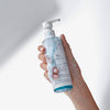 Eine Hand hält eine eingeschäumte Flasche Amphibien vor einem weißen Hintergrund.