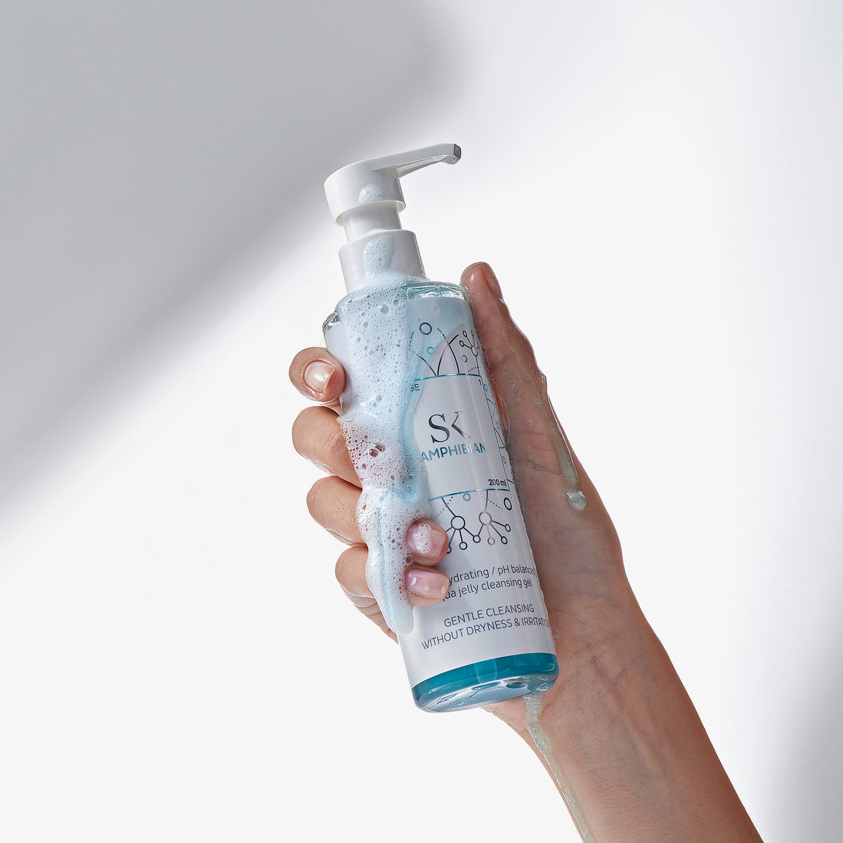 Eine Hand hält eine eingeschäumte Flasche Amphibien vor einem weißen Hintergrund.