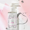 Eine Flasche Atomic-Reiniger mit Pumpspender und einen Flüssigkeitsspritzer auf rosa Hintergrund.