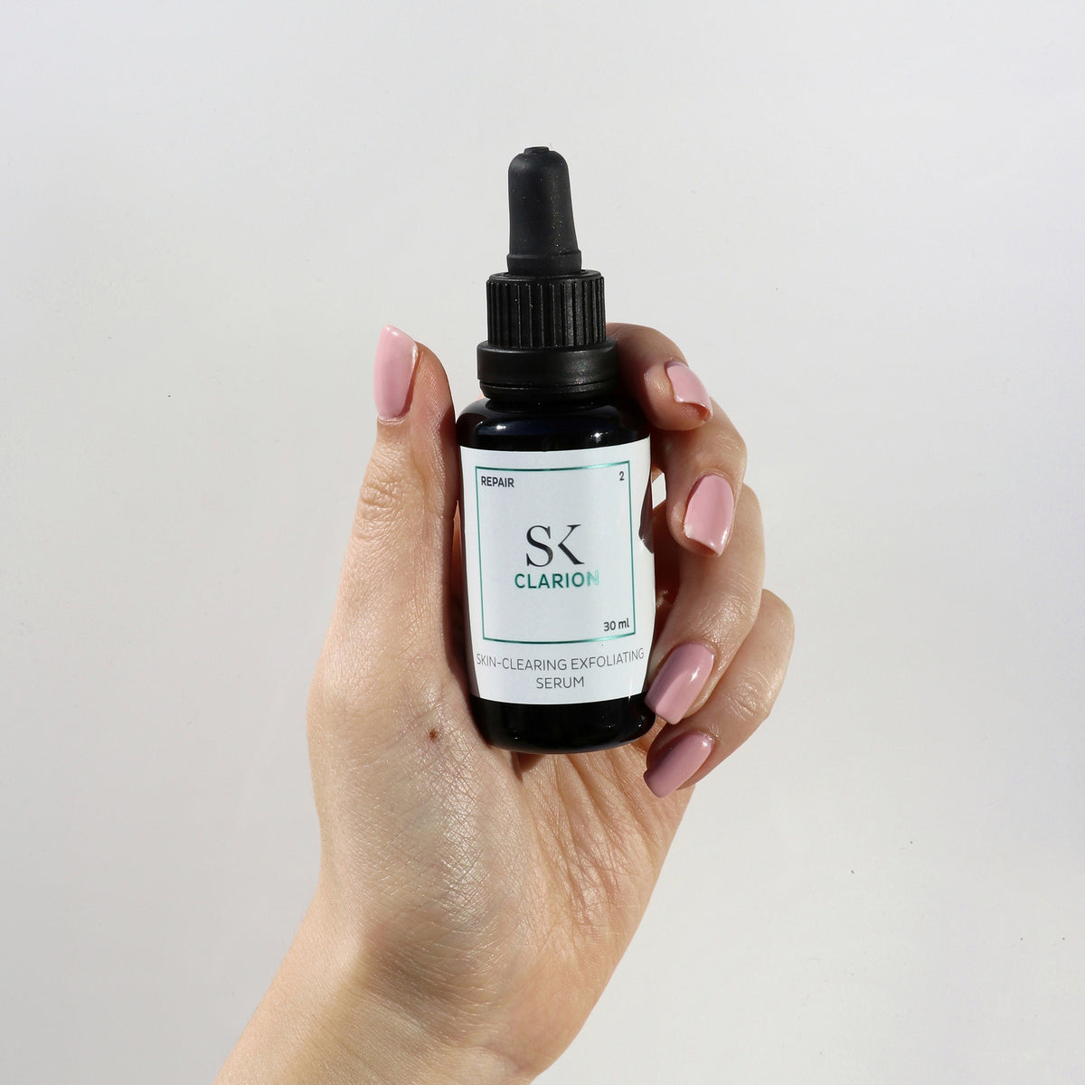 Hand hält eine Flasche Clarion-Peeling-Serum zur Hautreinigung vor einem schlichten weißen Hintergrund.
