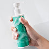 Hand hält grüne Flasche des Skintegra Clarion 2% BHA Cleansers mit Pumpspender, bedeckt mit Schaum.