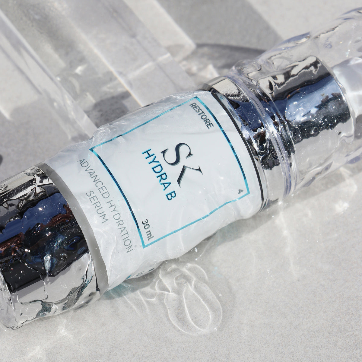 Nahaufnahme einer nassen Flasche Skintegra Hydra B Serum mit glänzender Oberfläche, liegend auf hellem Untergrund mit Wasserreflexionen.