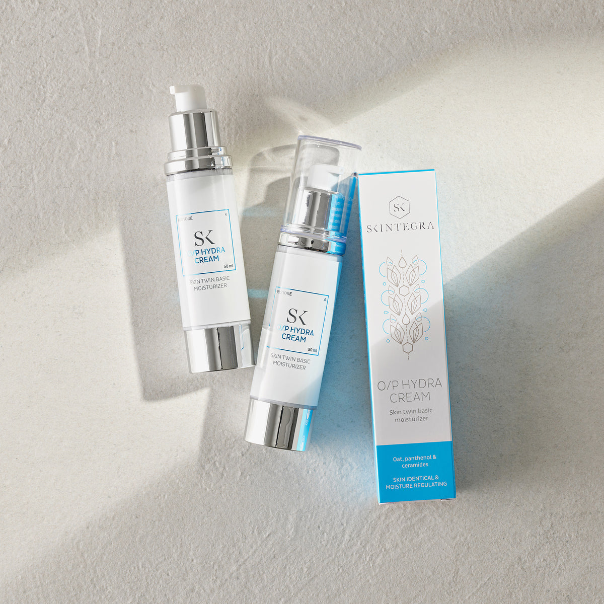 Zwei Flaschen O/P Hydra Cream mit passender Schachtel auf hellem Untergrund.