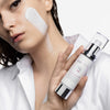 Frau mit aufgetragener Creme auf der Wange hält den Skintegra UNA Moisturizer in der Hand.