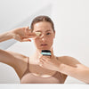 Junge Frau in beigem Top trägt mit zwei Fingern eine cremige Gesichtsmaske aus einem Tiegel „Volcanica“ auf, vor hellem, minimalistischem Hintergrund.