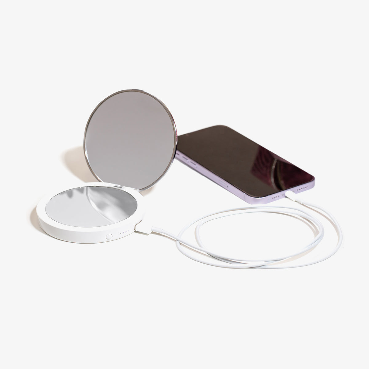 Der Flip n Charge Power Bank Compact LED Mirror mit weißem Kabel liegt neben einem lila Smartphone auf weißem Hintergrund.