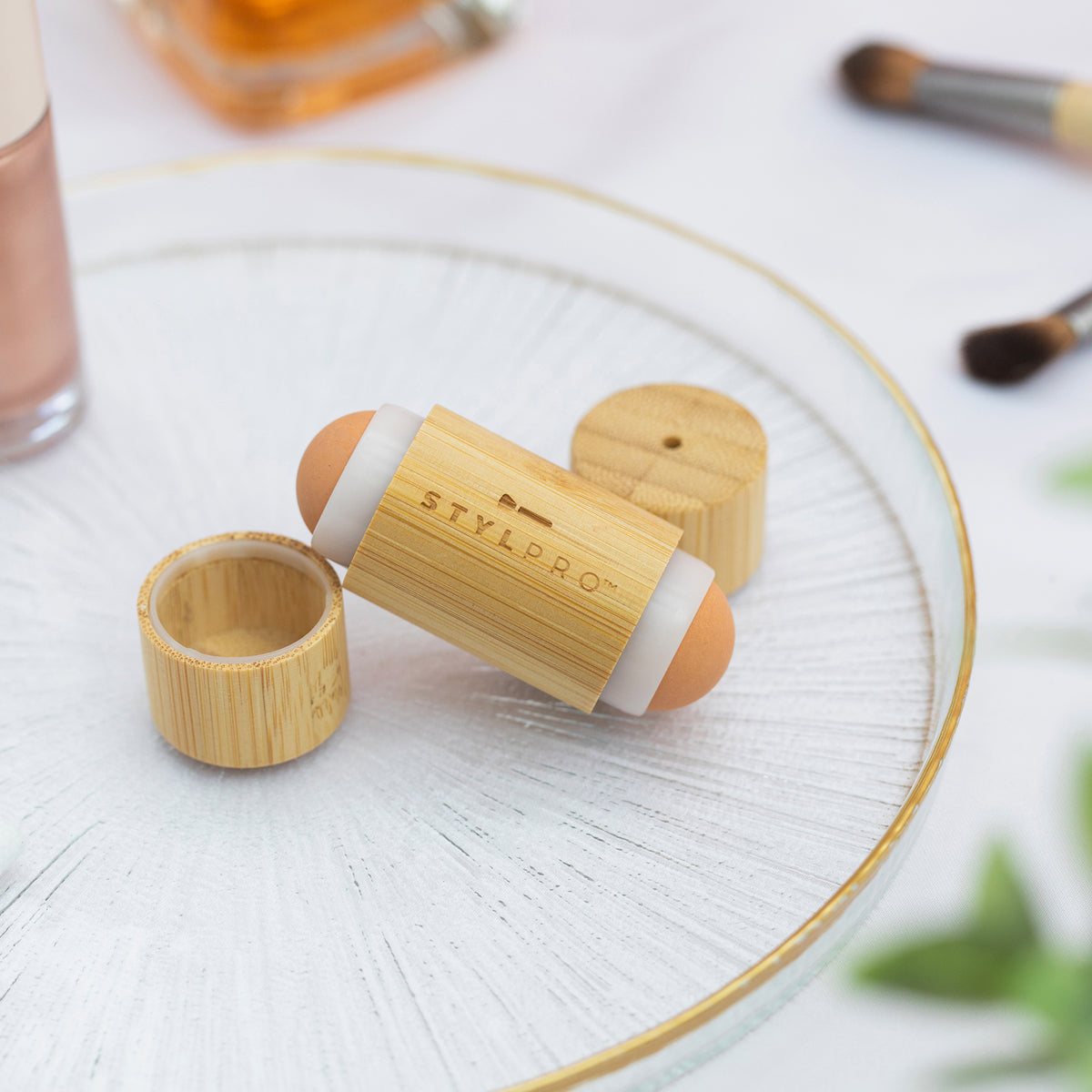 Bamboo Roller mit geöffneter Kappe auf einer Glasplatte, umgeben von Make-up-Artikeln.